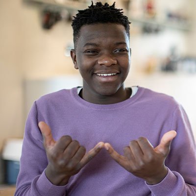 A teenage boy is shown signing in American Sign Language smiling. (Getty Images)