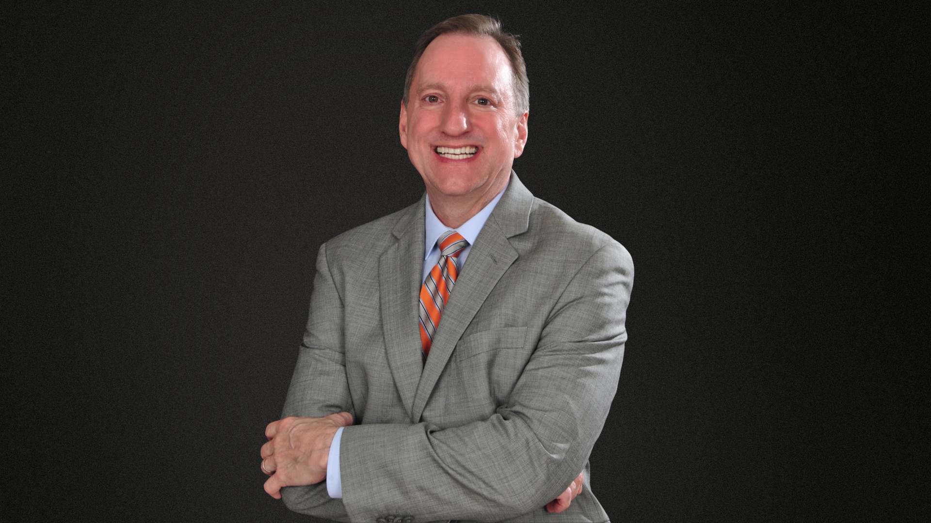 James Langabeer, Phd, in grey suit smiling with arms crossed