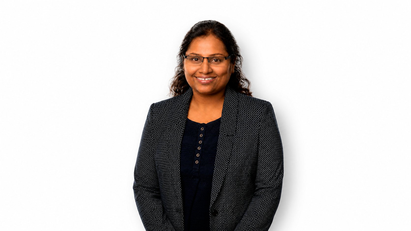 Professional studio headshot of a Asha Poulose Jhonson, with dark hair pulled back, wearing rectangular glasses, a navy patterned blazer over a dark blouse, against a white studio background.