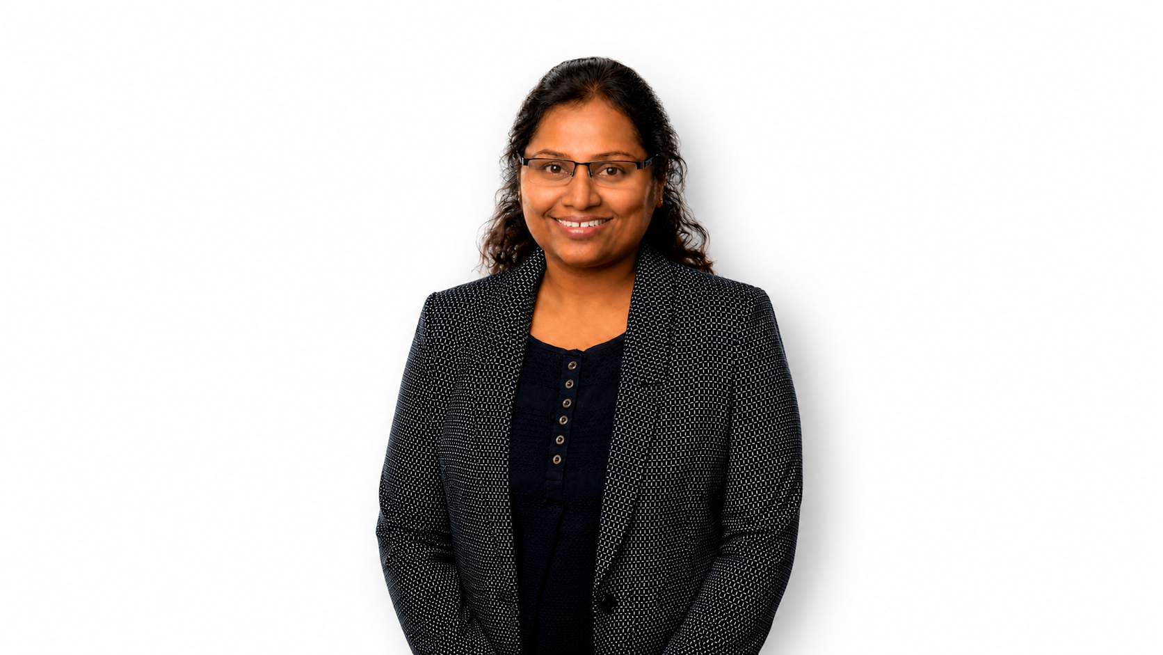 Professional studio headshot of a Asha Poulose Jhonson, with dark hair pulled back, wearing rectangular glasses, a navy patterned blazer over a dark blouse, against a white studio background.