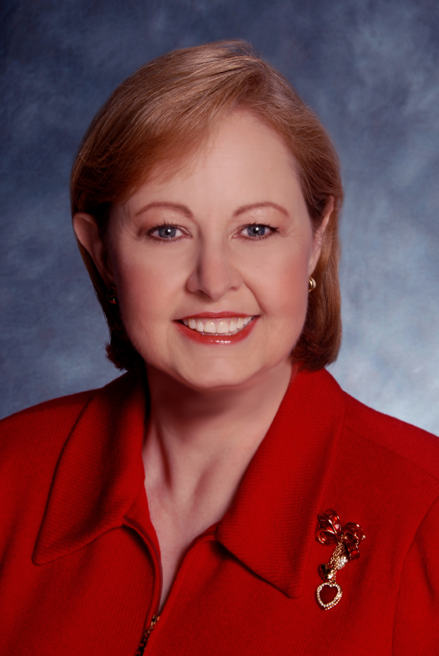 Head shot of Mellanie True Hills in red knit top with heart-shaped jewelled pendant